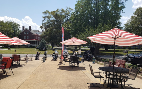 Outdoor seating area with striped umbrellas, motorcycles parked nearby, and a historic building in the background.