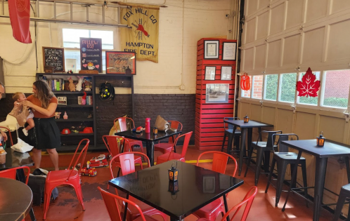 A cozy café interior with red chairs, black tables, and a woman interacting with a child near a display of local memorabilia.