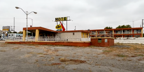 Abandoned motel with a large sign, surrounded by overgrown grass and a cloudy sky.