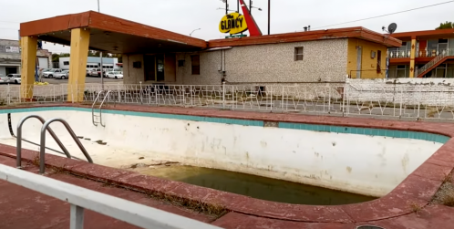 Abandoned motel with a dirty, empty swimming pool in the foreground and a faded "Glory" sign in the background.