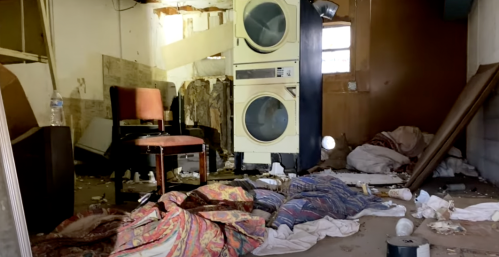 A cluttered, abandoned room with a chair, laundry machines, and scattered debris on the floor.