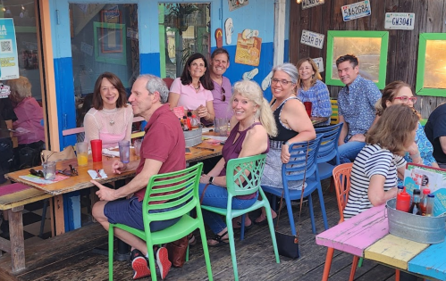A group of people sitting at a colorful outdoor restaurant, enjoying food and drinks, smiling and chatting together.