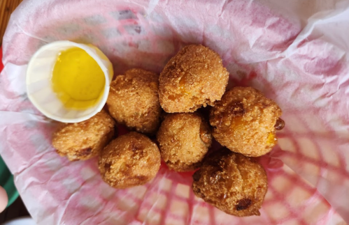 A basket of golden-brown fried balls with a small cup of yellow dipping sauce on the side.