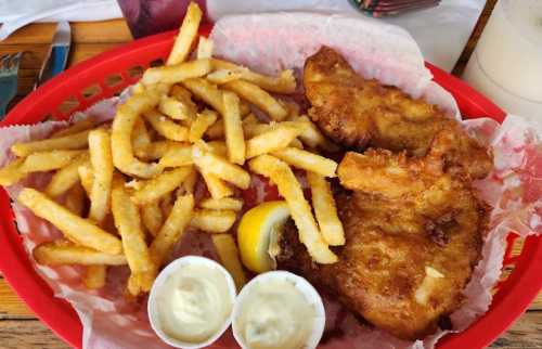A red basket filled with golden fried fish, crispy fries, a lemon wedge, and two cups of dipping sauce.