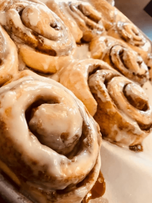 Freshly baked cinnamon rolls drizzled with creamy icing, arranged on a tray.