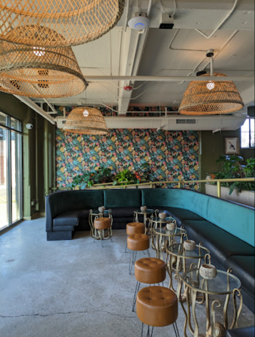 A stylish cafe interior featuring green walls, floral wallpaper, woven light fixtures, and modern seating.