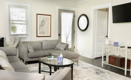 Cozy living room with gray sofas, a glass coffee table, artwork, and a door leading outside.