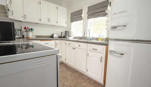 Bright kitchen with white cabinets, a black stove, and a vintage refrigerator, featuring natural light and tiled flooring.
