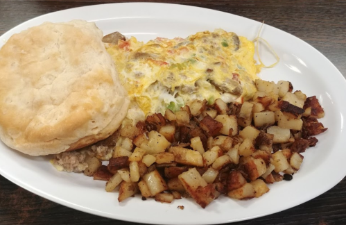 A plate of breakfast featuring a biscuit, cheesy scrambled eggs with vegetables, and seasoned diced potatoes.