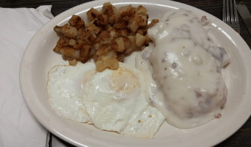 A plate with three fried eggs, creamy sausage gravy over biscuits, and crispy hash browns on the side.
