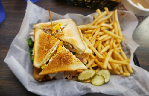 A toasted sandwich with lettuce, cheese, and pickles, served with a side of golden French fries on parchment paper.