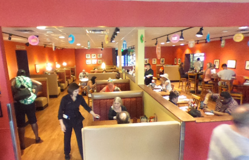 A busy restaurant interior with patrons in booths and at tables, and a server attending to customers.
