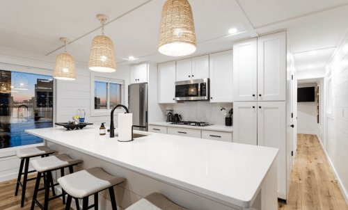 Modern kitchen with white cabinets, a large island, pendant lights, and a view of the city skyline through a window.