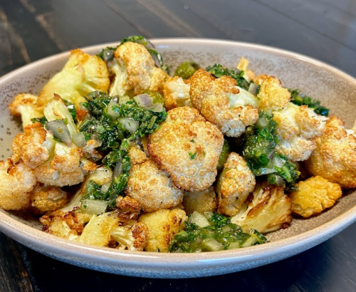 A bowl of roasted cauliflower mixed with herbs and spices, garnished with green vegetables.