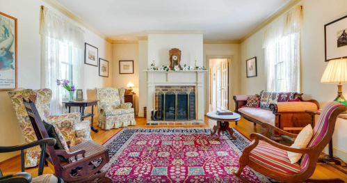 Cozy living room with floral armchairs, a fireplace, and a patterned rug, featuring warm lighting and decorative accents.