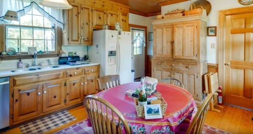 Cozy kitchen with wooden cabinets, a round table set for dining, and a door leading outside. Warm, inviting atmosphere.