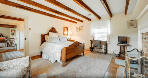 Cozy bedroom with wooden beams, a vintage bed, desk, and soft lighting, featuring warm decor and a welcoming atmosphere.