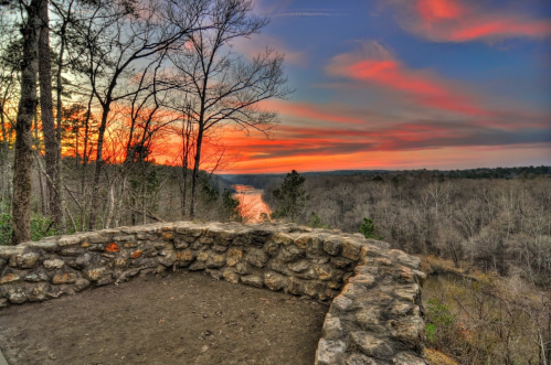 A scenic view from a stone overlook at sunset, with vibrant colors in the sky and a river winding through the landscape.
