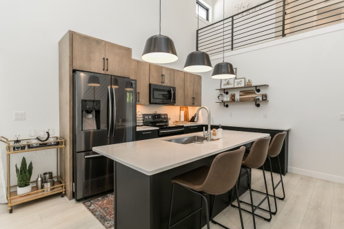 Modern kitchen with black appliances, a large island, bar stools, and stylish pendant lighting. Bright and spacious design.