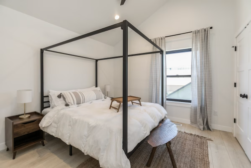 A modern bedroom featuring a four-poster bed, light bedding, and a cozy atmosphere with natural light.
