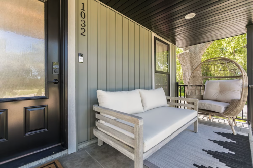 A cozy porch with a wooden bench, a hanging chair, and a modern door, surrounded by greenery.