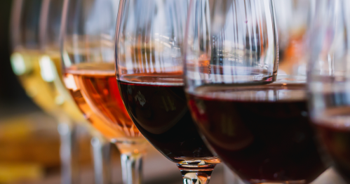 A row of wine glasses filled with red, white, and rosé wines, reflecting light in a warm setting.