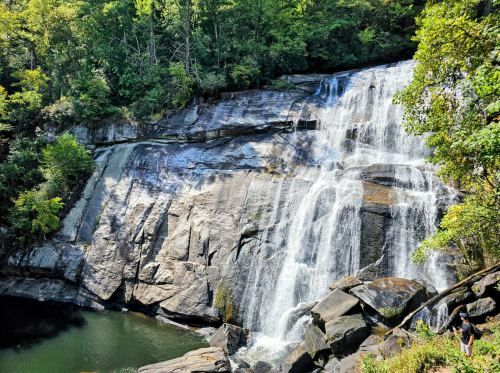 A serene waterfall cascades over rocky cliffs into a calm pool, surrounded by lush green trees.