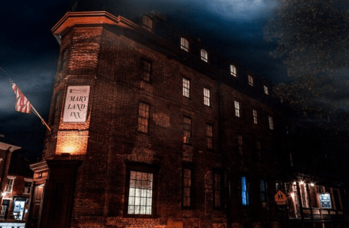 A historic brick building, the Maryland Inn, illuminated at night with a cloudy sky above.