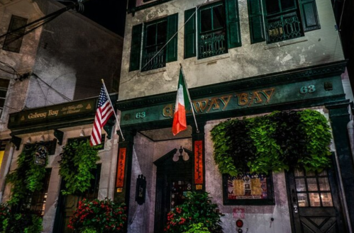A historic building at night with an American flag and an Italian flag, adorned with greenery and flowers.
