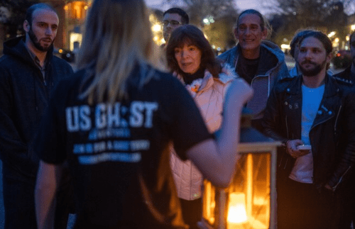 A group of people gathered around a guide holding a lantern during a nighttime tour.