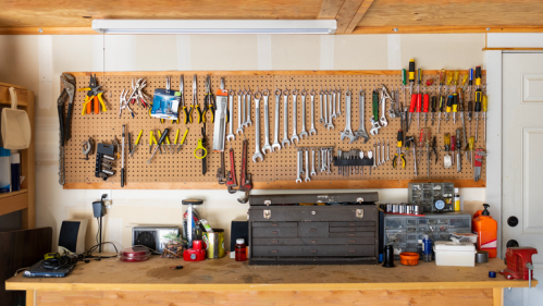 A well-organized workshop with tools hanging on a pegboard and a wooden workbench cluttered with various items.