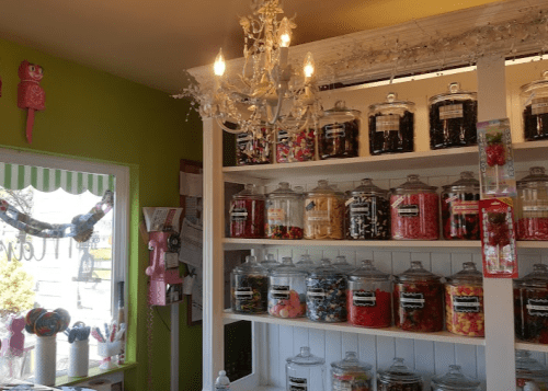 A colorful candy shop interior with jars of sweets on shelves and a chandelier overhead.