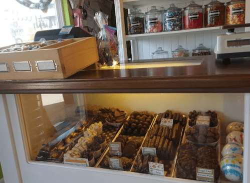 A display case filled with various chocolates and candies, with jars of sweets in the background.