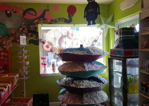 Colorful candy shop interior featuring a tiered display of taffy, vibrant wall art, and various sweets.
