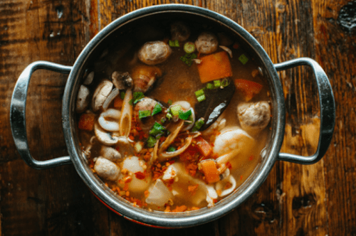 A pot of flavorful seafood soup with vegetables and herbs, set on a rustic wooden table.