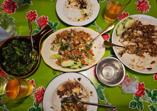 A vibrant table spread with various dishes, including rice, vegetables, and a salad, surrounded by drinks.