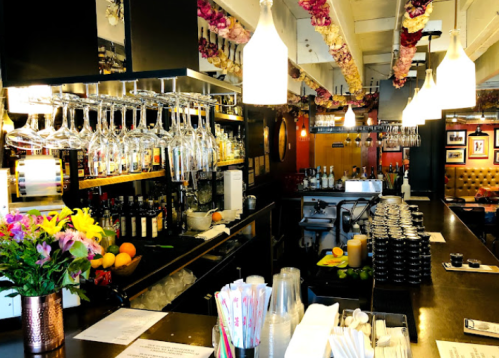 A stylish bar with hanging glasses, colorful flowers, and a variety of drinks on display.
