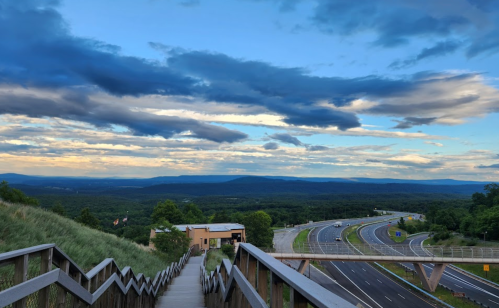 A scenic view from a wooden staircase overlooking a highway and lush green landscape under a cloudy sky.
