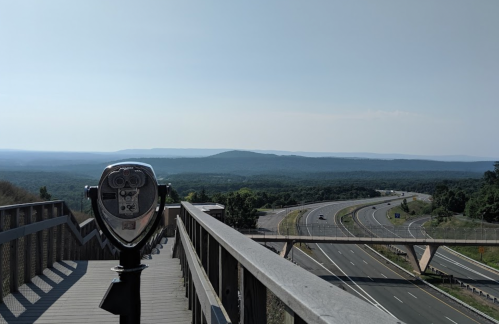 View from a lookout point featuring a coin-operated binocular viewer and a highway winding through green hills.