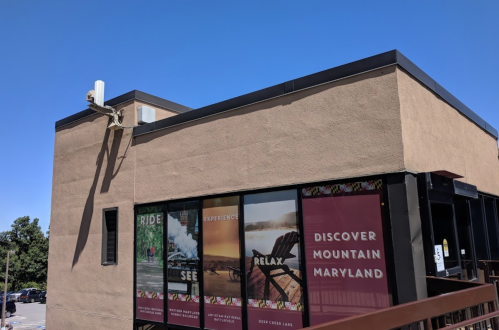 A building with large windows displaying promotional signs for activities in Mountain Maryland, under a clear blue sky.