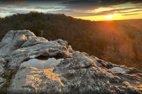 Sunset over a rocky landscape, with a small pool of water reflecting the warm colors of the sky.