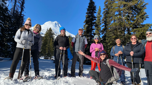 A group of people poses in the snow with mountains in the background, enjoying a sunny day outdoors.