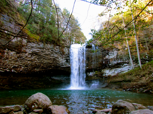 A serene waterfall cascades into a clear pool, surrounded by rocky cliffs and lush greenery.