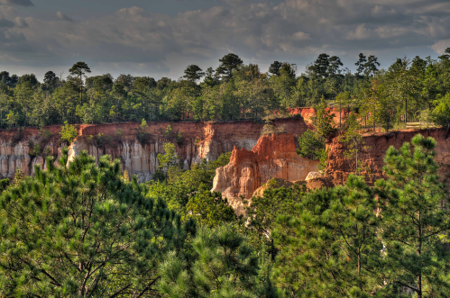 A scenic view of rugged cliffs surrounded by lush green trees under a partly cloudy sky.