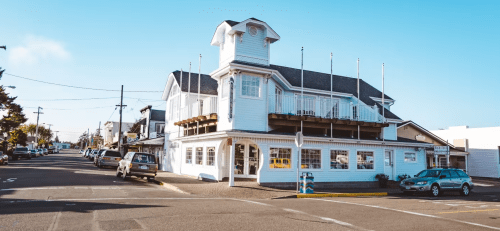 A charming white building with a tower, located at a street corner, surrounded by parked cars and clear blue skies.