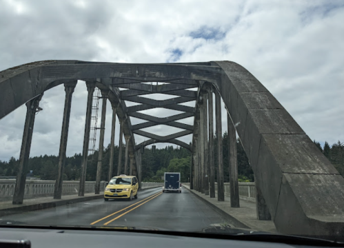 A view from a car driving over a large, arched concrete bridge with a yellow taxi and a truck ahead.