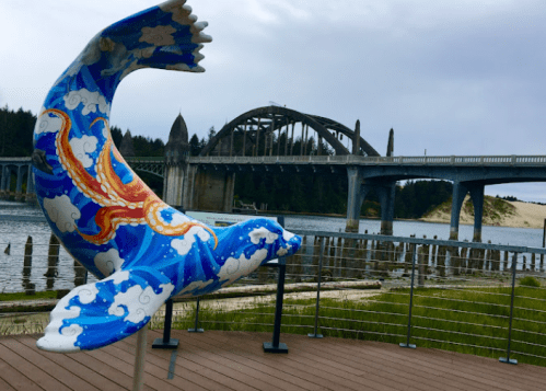 A colorful whale sculpture near a bridge, with a river and forested hills in the background.
