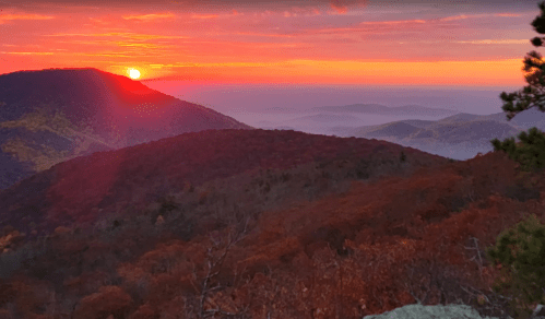 A vibrant sunset over rolling mountains, with autumn foliage in shades of red and orange.