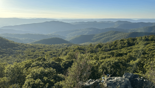 A panoramic view of rolling green mountains under a clear sky, with layers of hills fading into the distance.