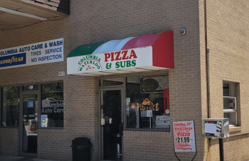 Sign for "Columbia Pizza & Subs" with a red, green, and white awning on a brick building. Nearby auto care service visible.